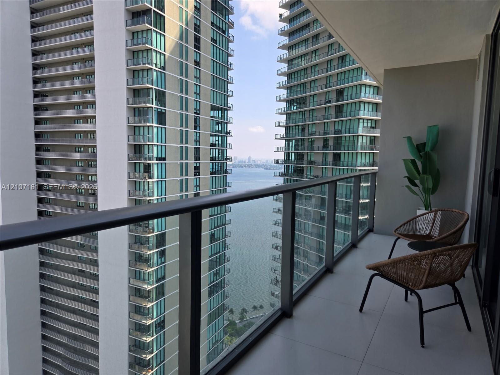 Private balcony featuring large-format tile flooring and a glass-paneled railing with a dark metal frame, overlooking an expanse of water