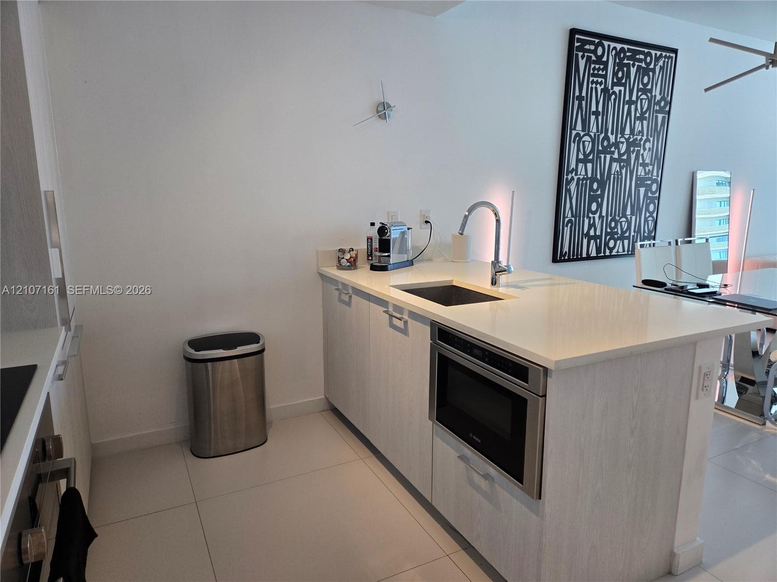 Modern kitchen featuring light wood-finish cabinetry, a stainless steel sink with contemporary faucet, and integrated stainless steel appliances including a microwave