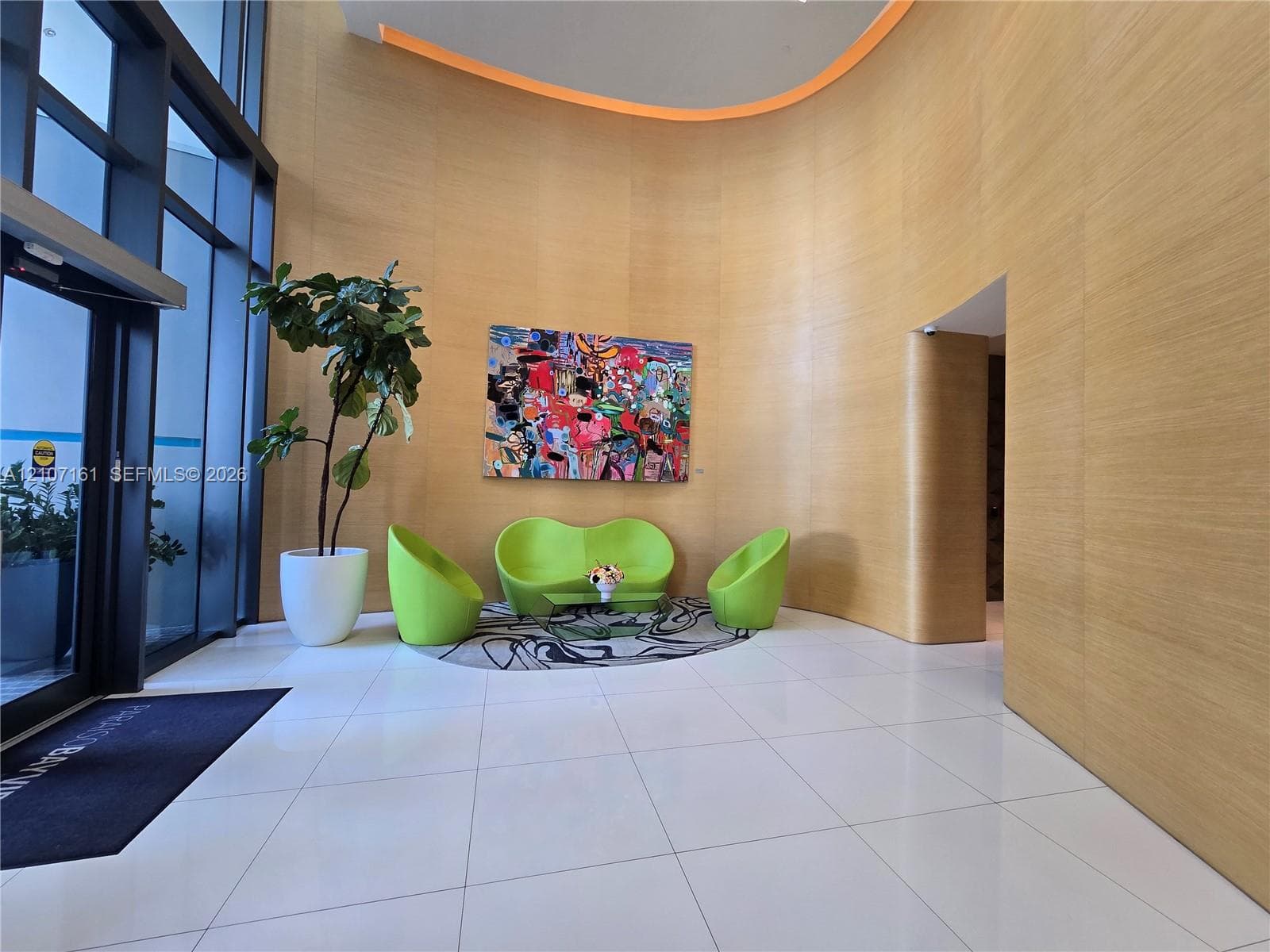 Double-height lobby featuring floor-to-ceiling glass paneling, curved wood-finish wall paneling, tile flooring, and integrated accent lighting