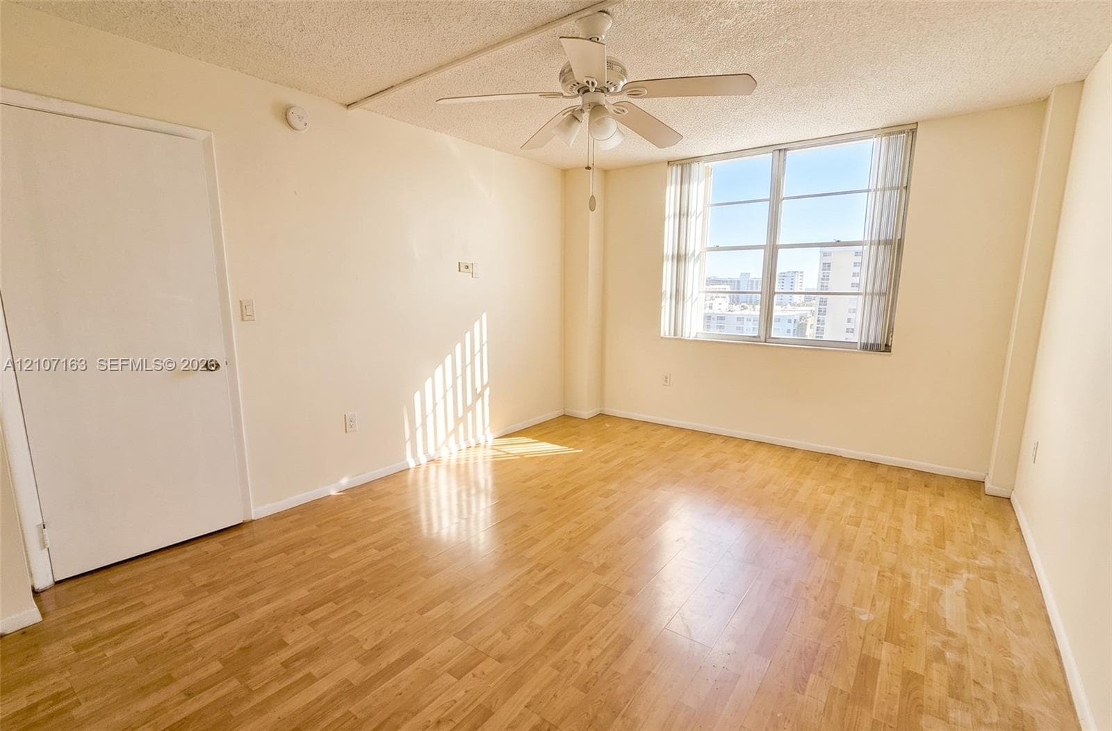 Interior space featuring wood-finish flooring, a multi-blade ceiling fan with integrated lighting, and a large multi-pane window with vertical blinds