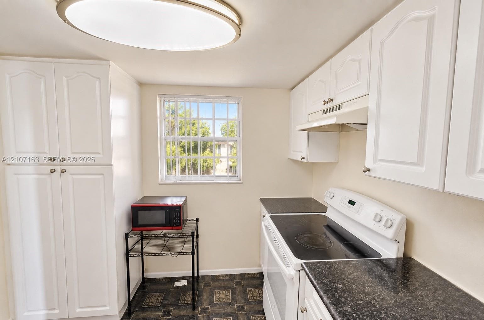Kitchen featuring white cabinetry, dark countertops, a built-in range, and a flush-mount circular ceiling light fixture