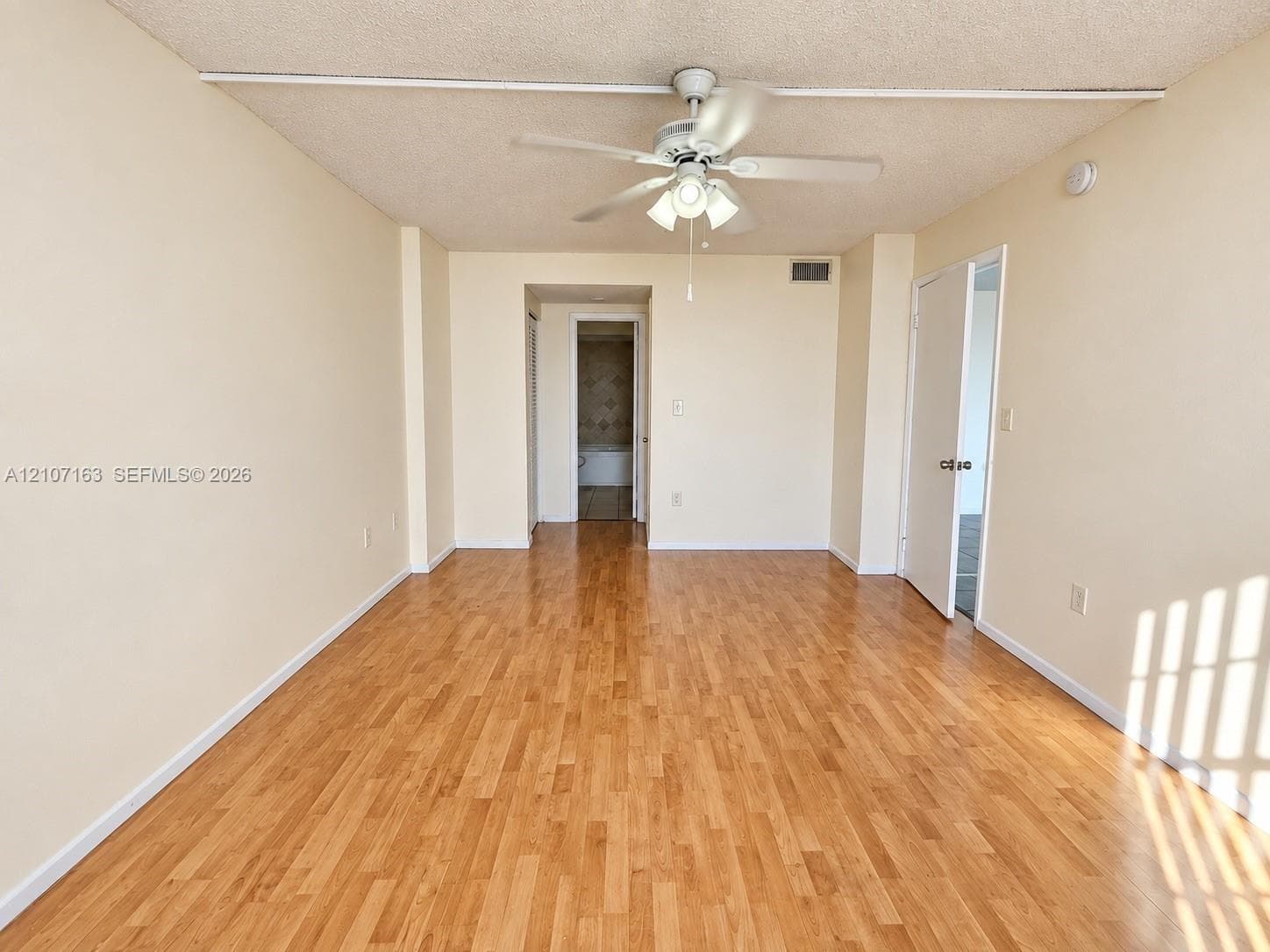 Room featuring wood-finish flooring, a central ceiling fan with integrated lighting, textured ceiling, and double-door entry
