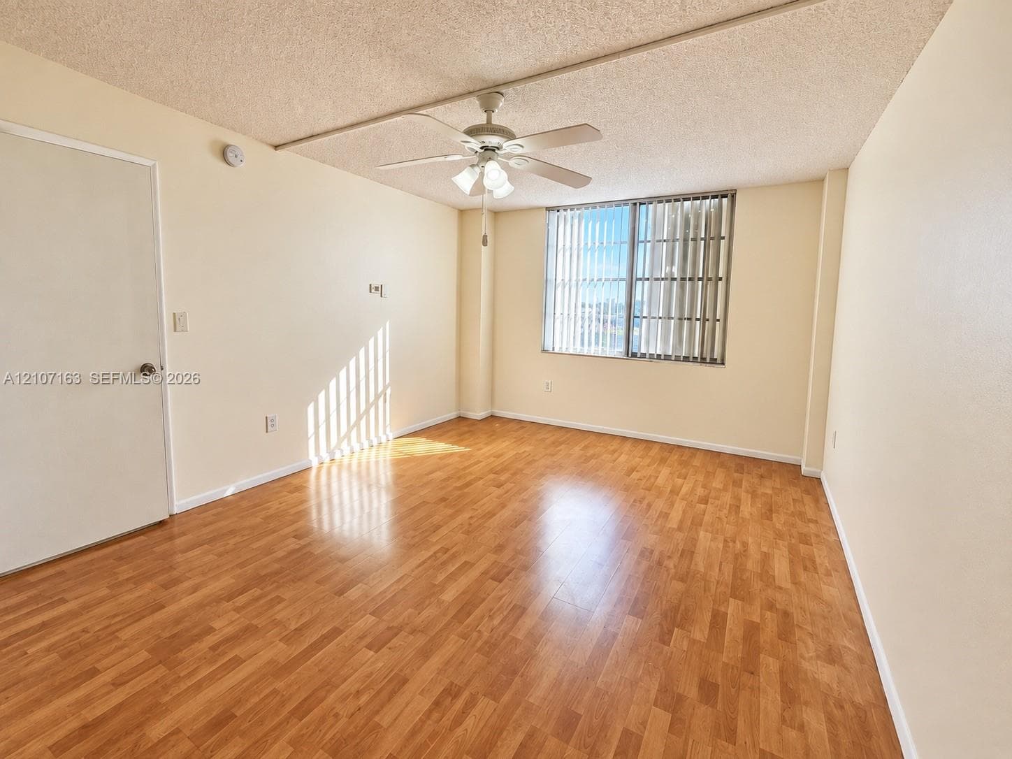 Interior space featuring wood-finish flooring, a ceiling fan with integrated lighting, and vertical window blinds