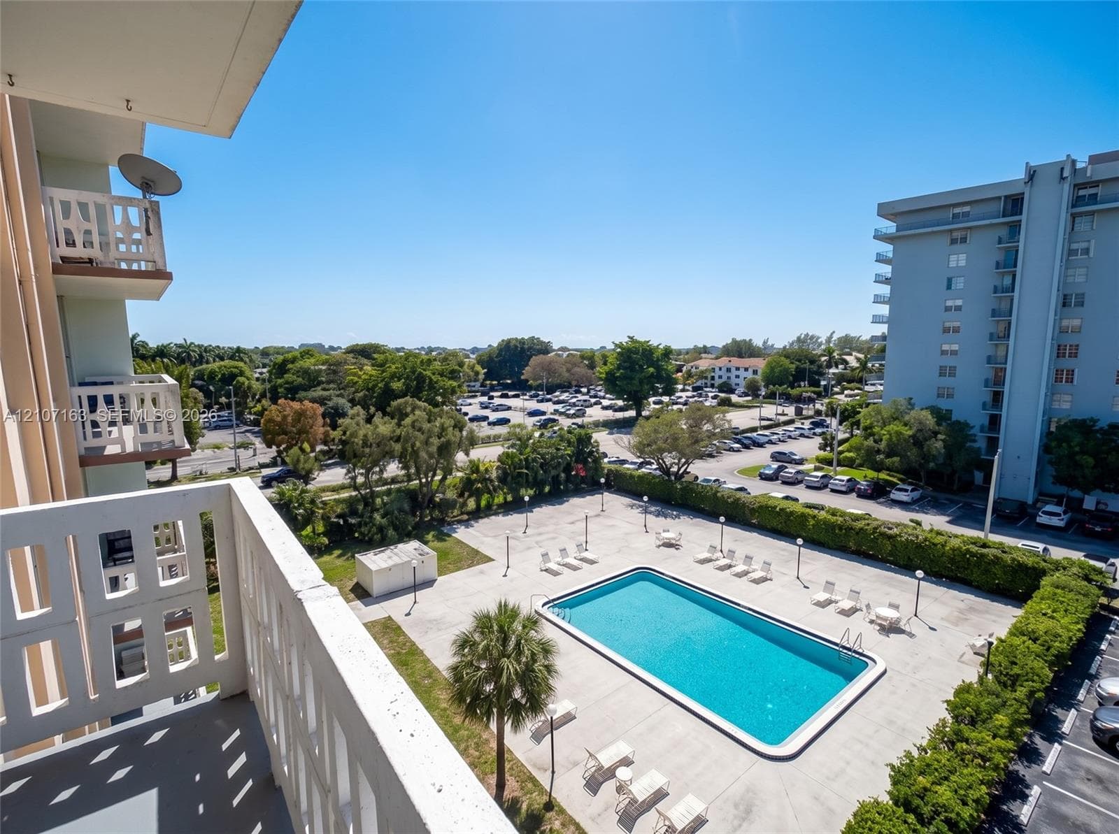 Private balcony with decorative masonry railing overlooking an outdoor swimming pool and paved deck area