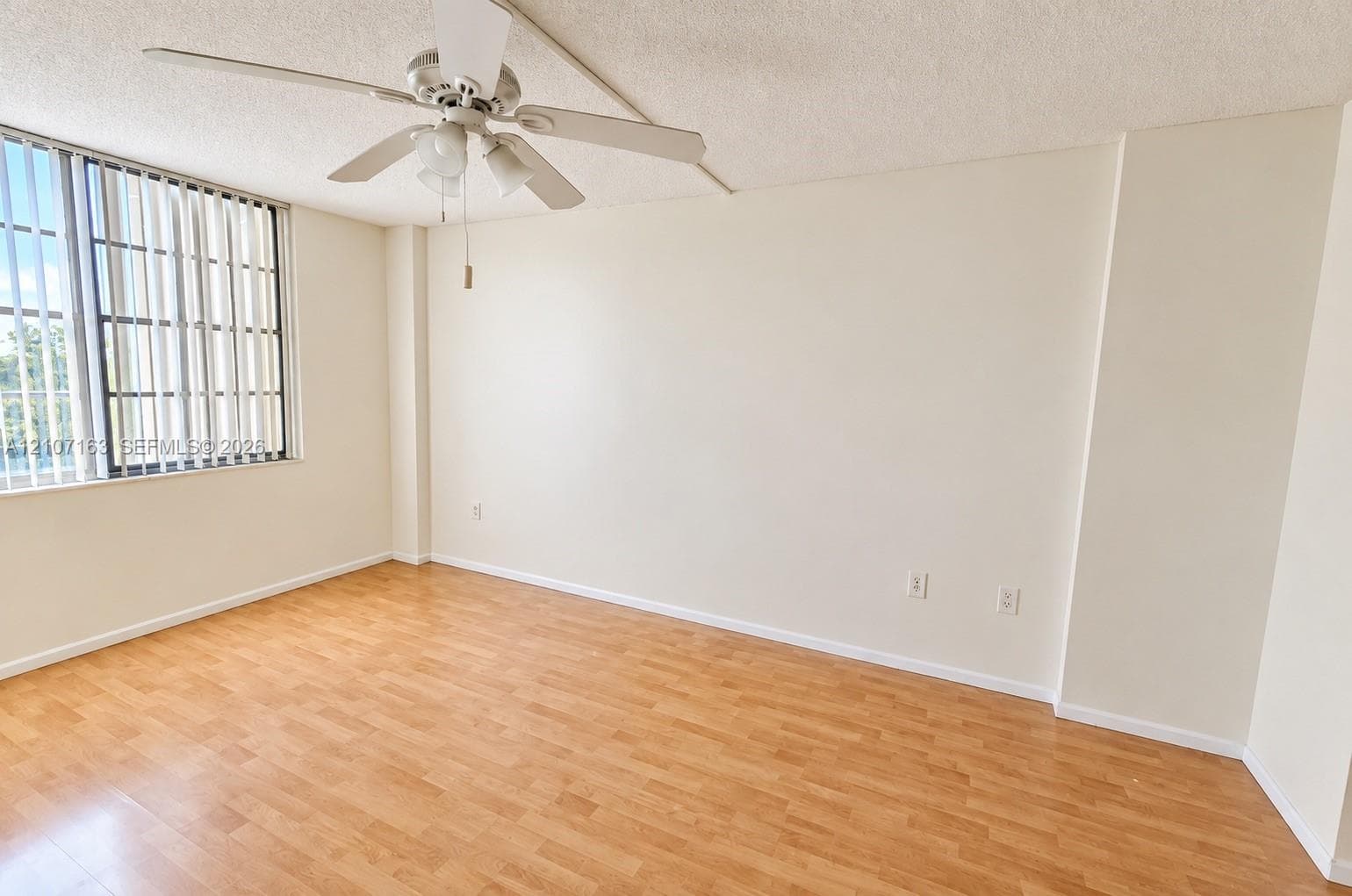 Room featuring wood-finish flooring, a ceiling fan with integrated lighting, and vertical window blinds