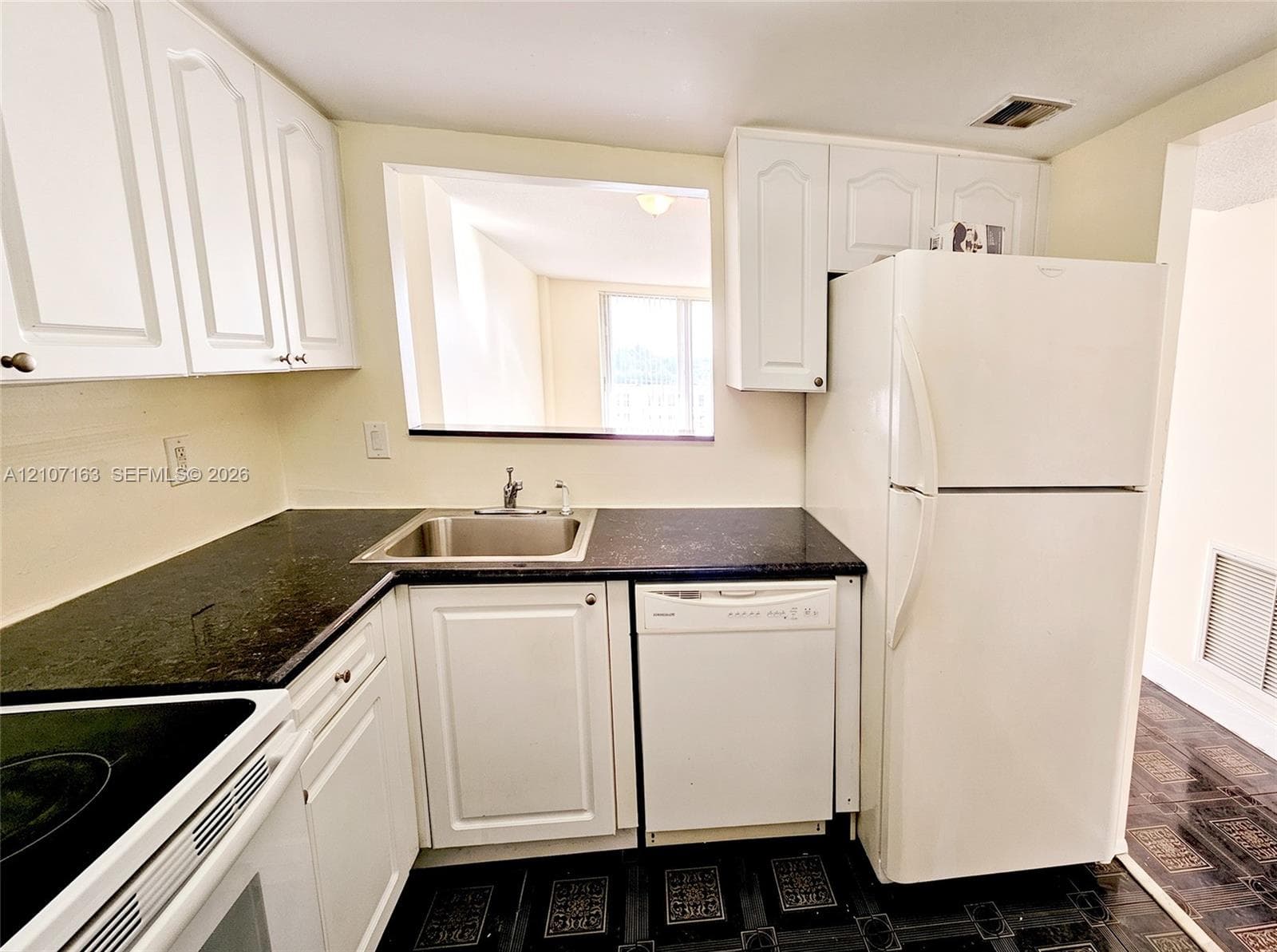 Kitchen featuring white shaker-style cabinetry, dark stone-finish countertops, stainless steel sink with a high-arch faucet, integrated dishwasher, and a full-size refrigerator