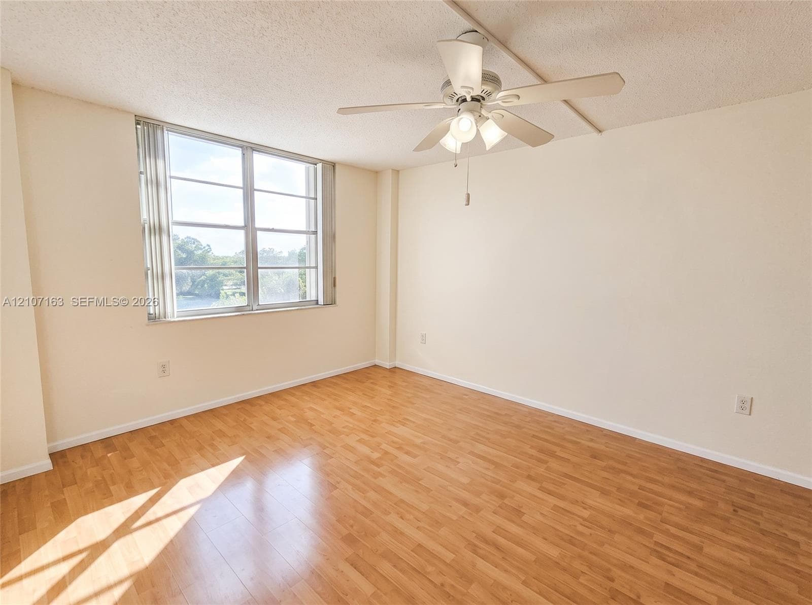 Wood-finish flooring, large window with vertical blinds, and a multi-blade ceiling fan with integrated lighting