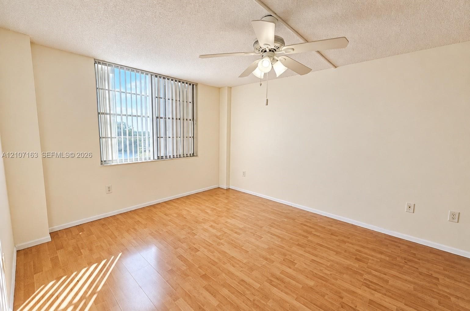 Interior space featuring wood-finish flooring, a ceiling fan with integrated lighting, and a large window with vertical blinds