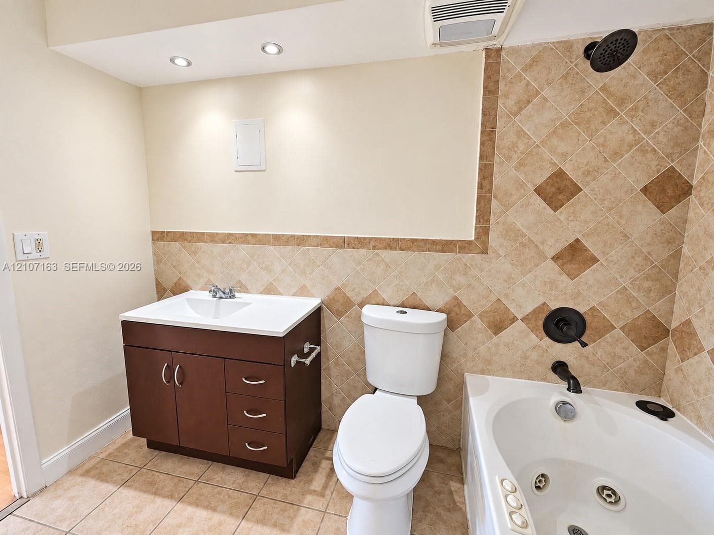 Bathroom featuring a dark wood-finish vanity with a white countertop, ceramic tile flooring, a jetted soaking tub, and stone-tile wall accents