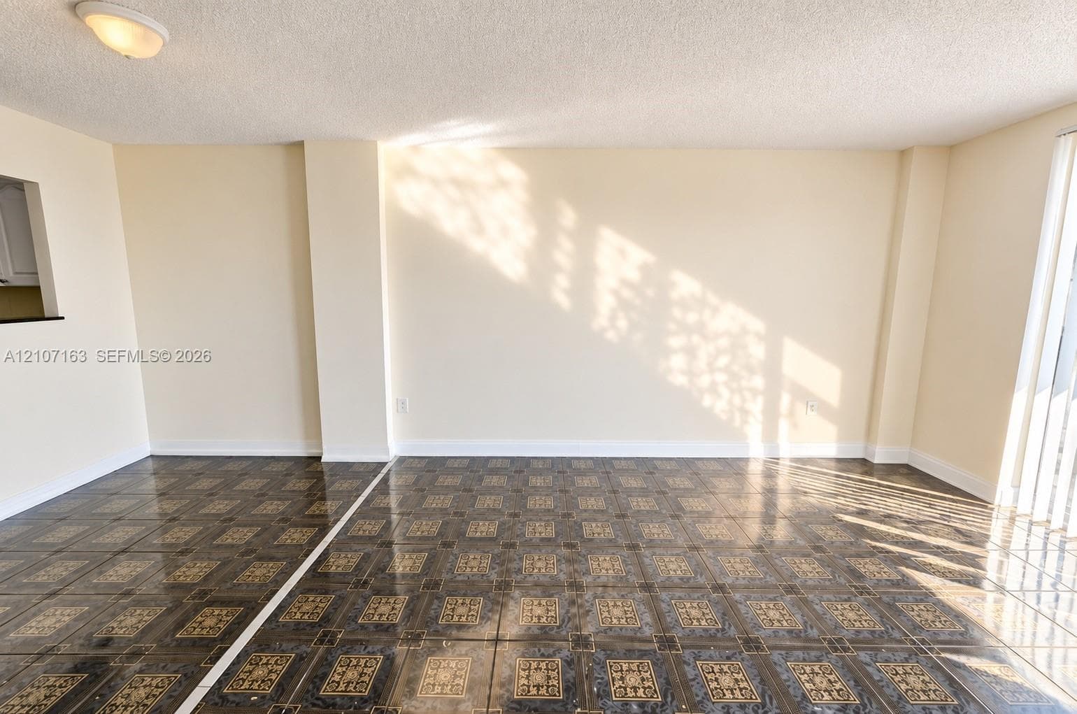 Interior space featuring patterned ceramic tile flooring, neutral wall tones, textured ceiling finish, flush-mount lighting, and a pass-through wall opening