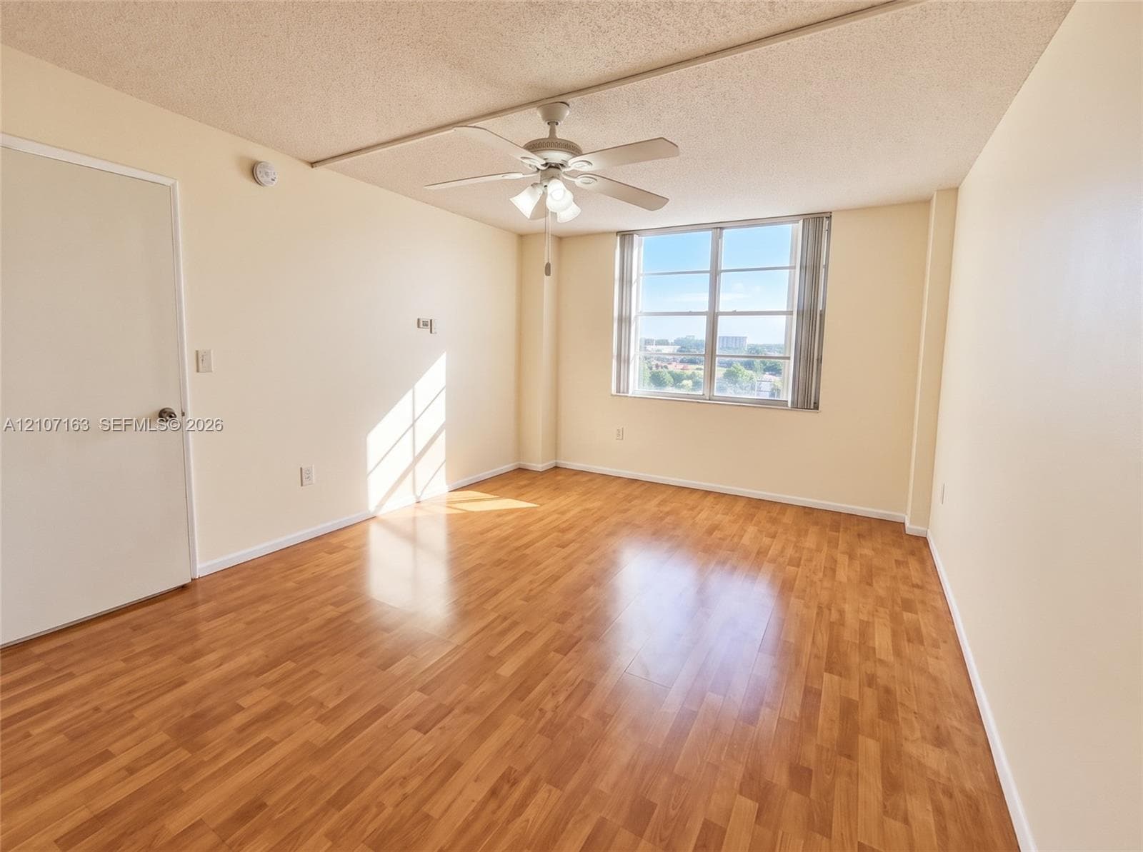 Wood-finish flooring, multi-pane window with vertical blinds, and ceiling fan with integrated lighting