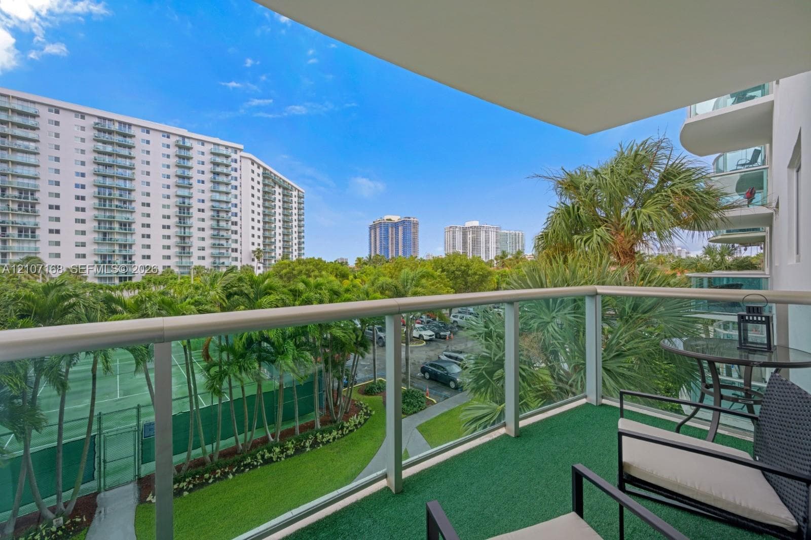 Private balcony featuring a glass-panel railing and green synthetic turf flooring