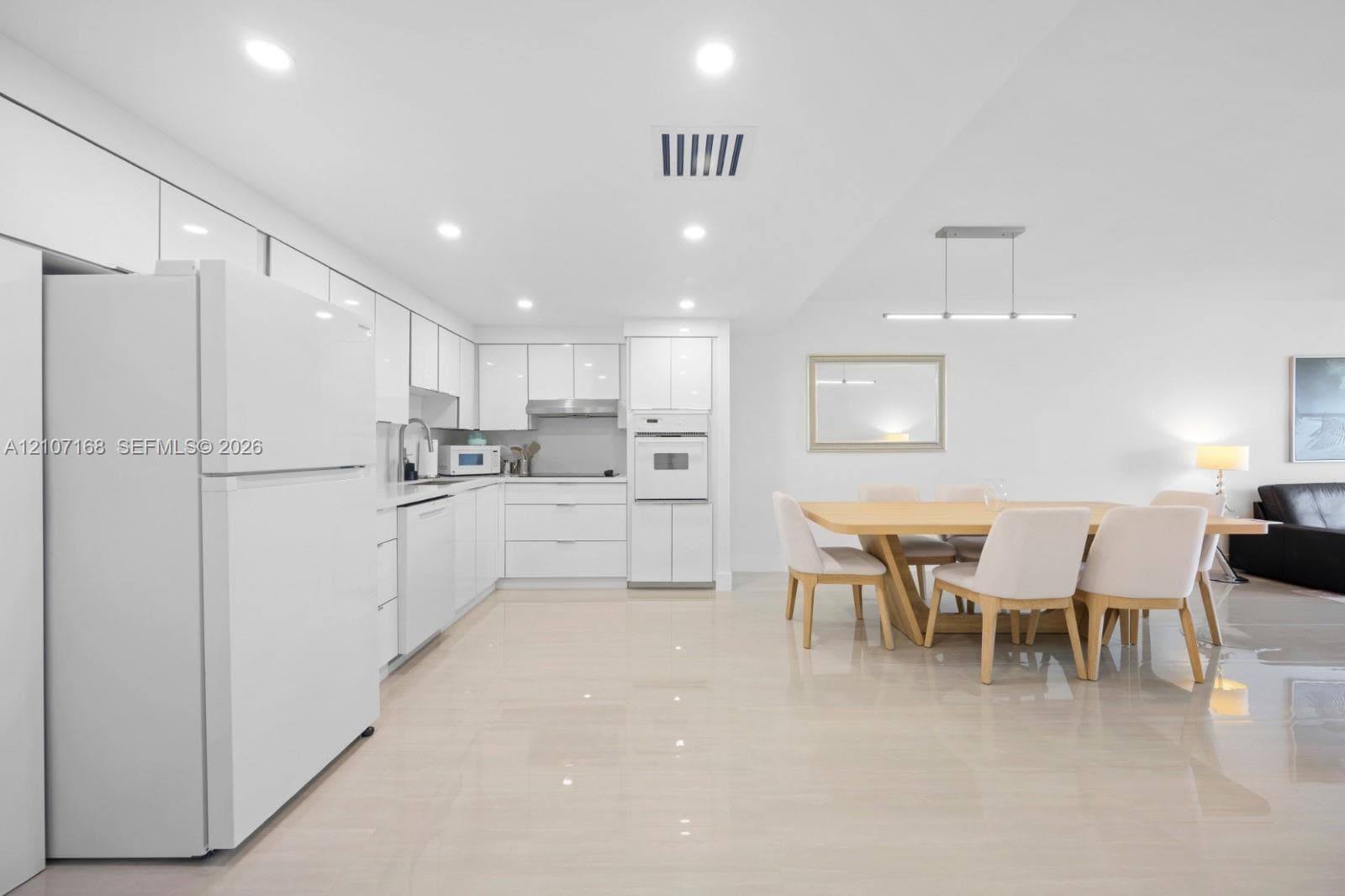 Contemporary kitchen featuring high-gloss white cabinetry, integrated appliances, recessed lighting, and polished tile flooring