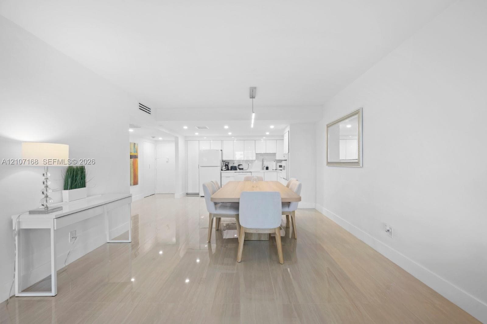 Open-concept interior featuring light-toned wood-finish flooring, high-gloss white cabinetry, recessed ceiling lighting, and a linear pendant light fixture