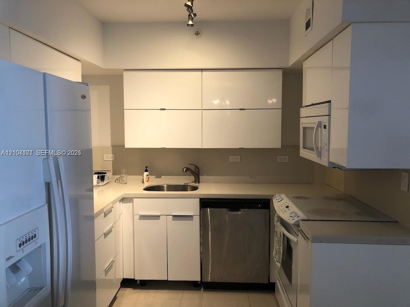 Kitchen featuring high-gloss white cabinetry, solid surface countertops, stainless steel undermount sink, and integrated stainless steel dishwasher