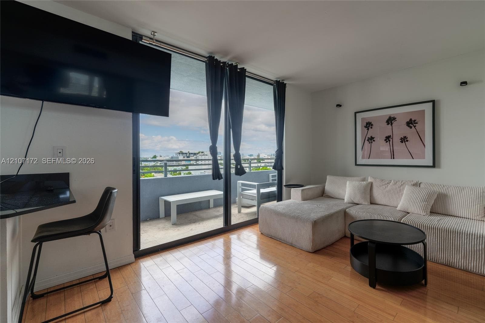 Floor-to-ceiling sliding glass doors, private balcony, wood-finish flooring, and wall-mounted lighting