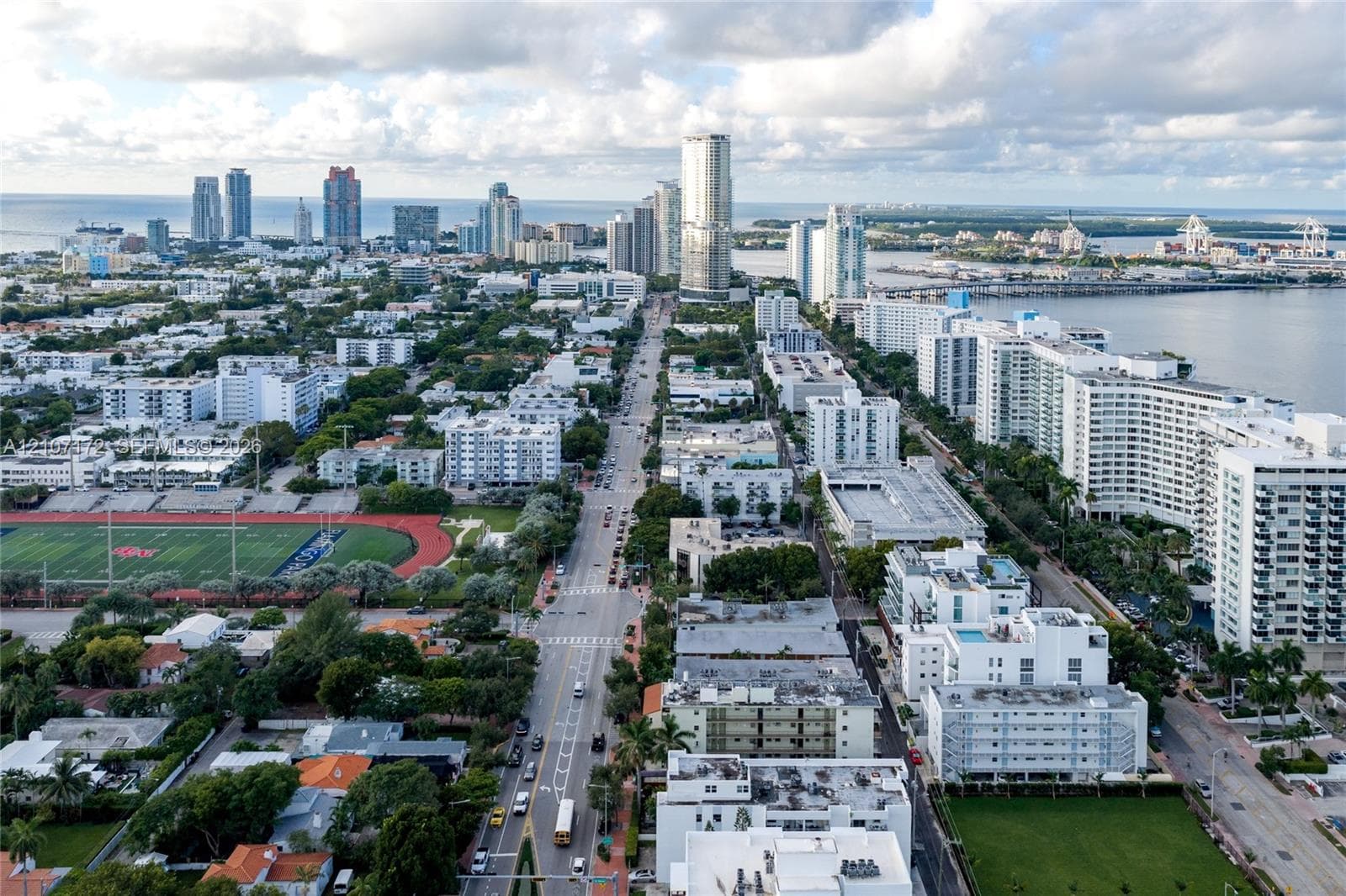 Aerial perspective showcasing a coastal metropolitan landscape, high-rise urban density, integrated athletic track facility, and proximity to shoreline waterways