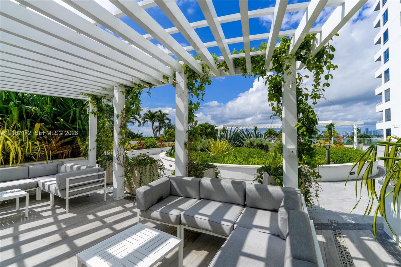 Rooftop terrace featuring an expansive white pergola, stone-tile flooring, and built-in masonry planters with integrated landscaping