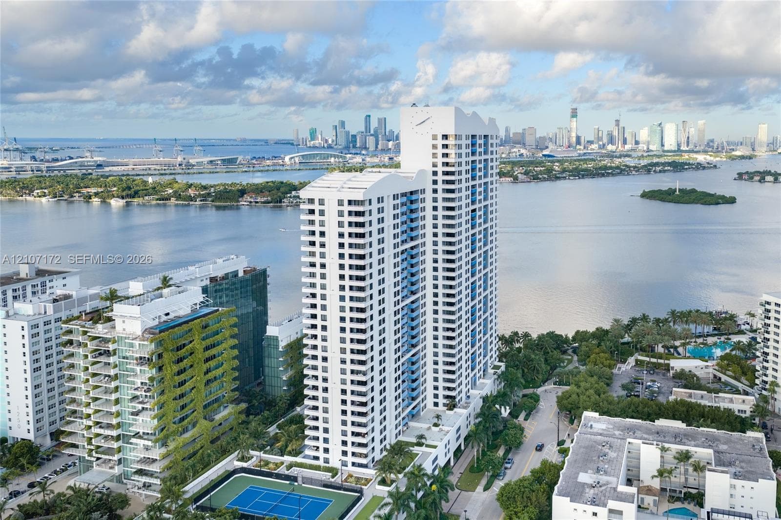 High-rise residential tower featuring white structural facade, tiered balcony design, onsite tennis court, and immediate waterfront positioning
