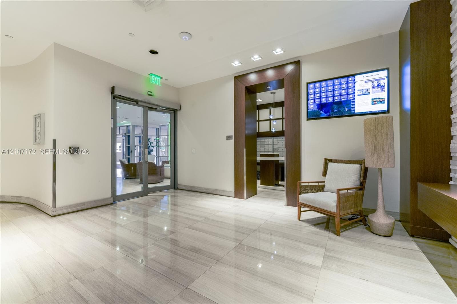 Lobby area featuring polished large-format stone-finish tile flooring, glass entry doors, recessed ceiling lighting, and a dark wood-trim architectural portal
