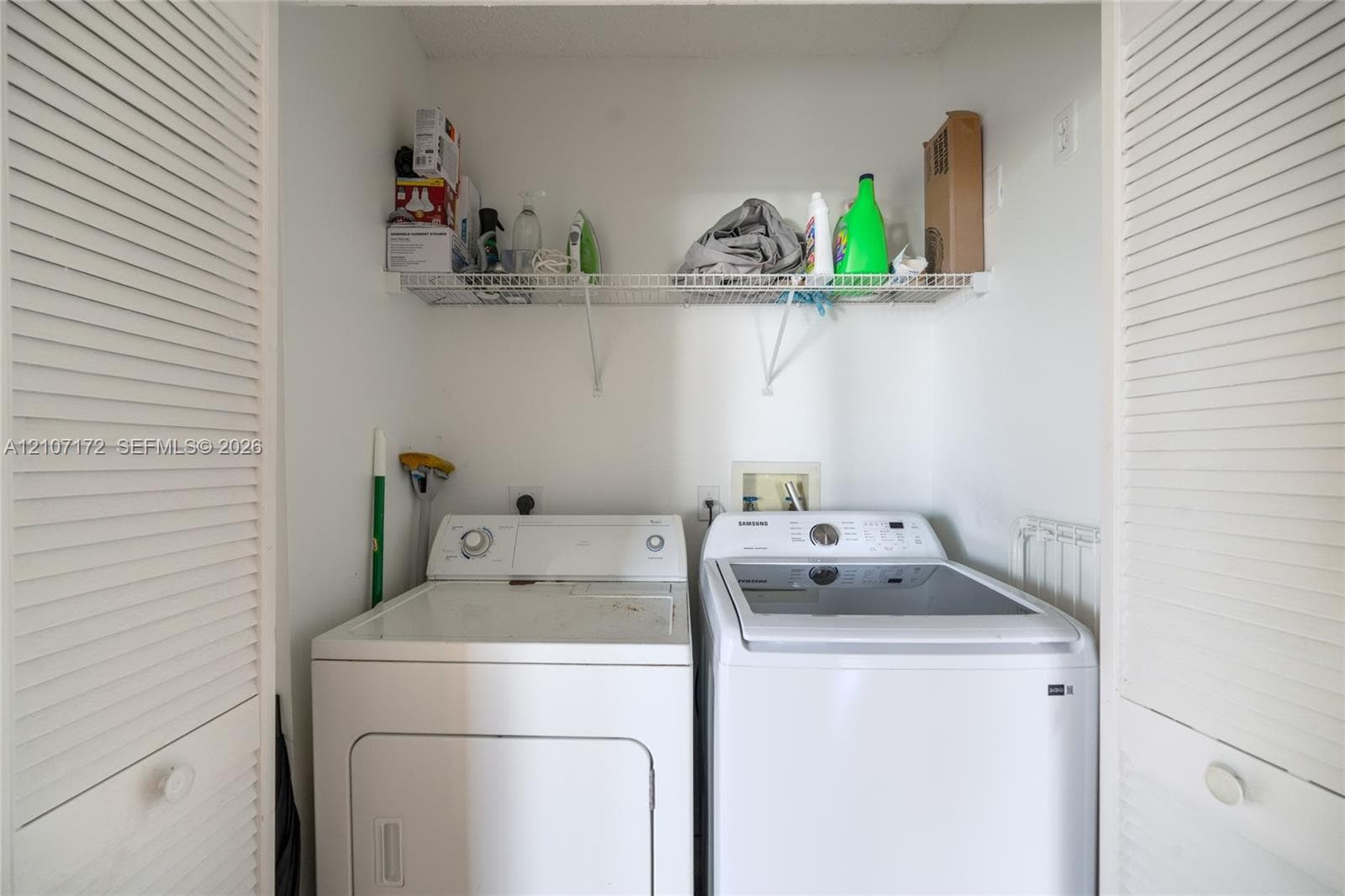 Laundry closet featuring white louvered doors and an elevated wire shelving unit