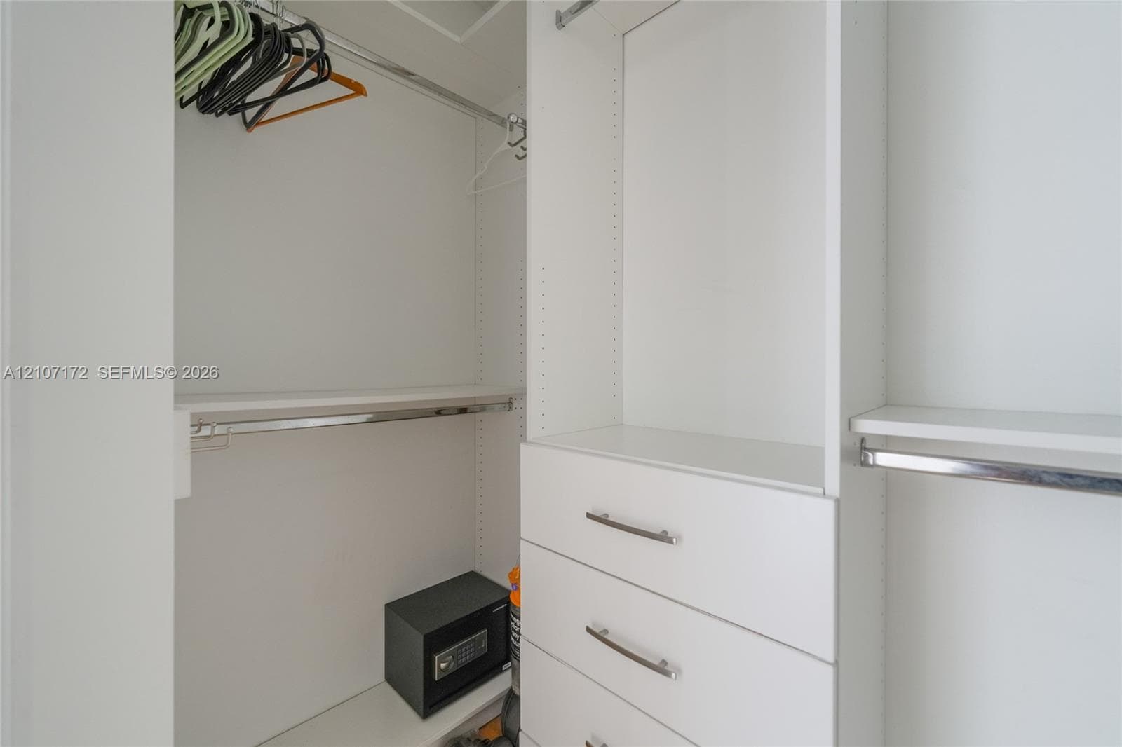Built-in closet system featuring white cabinetry, integrated shelving, tiered hanging rods, and a stack of three drawers with metallic hardware