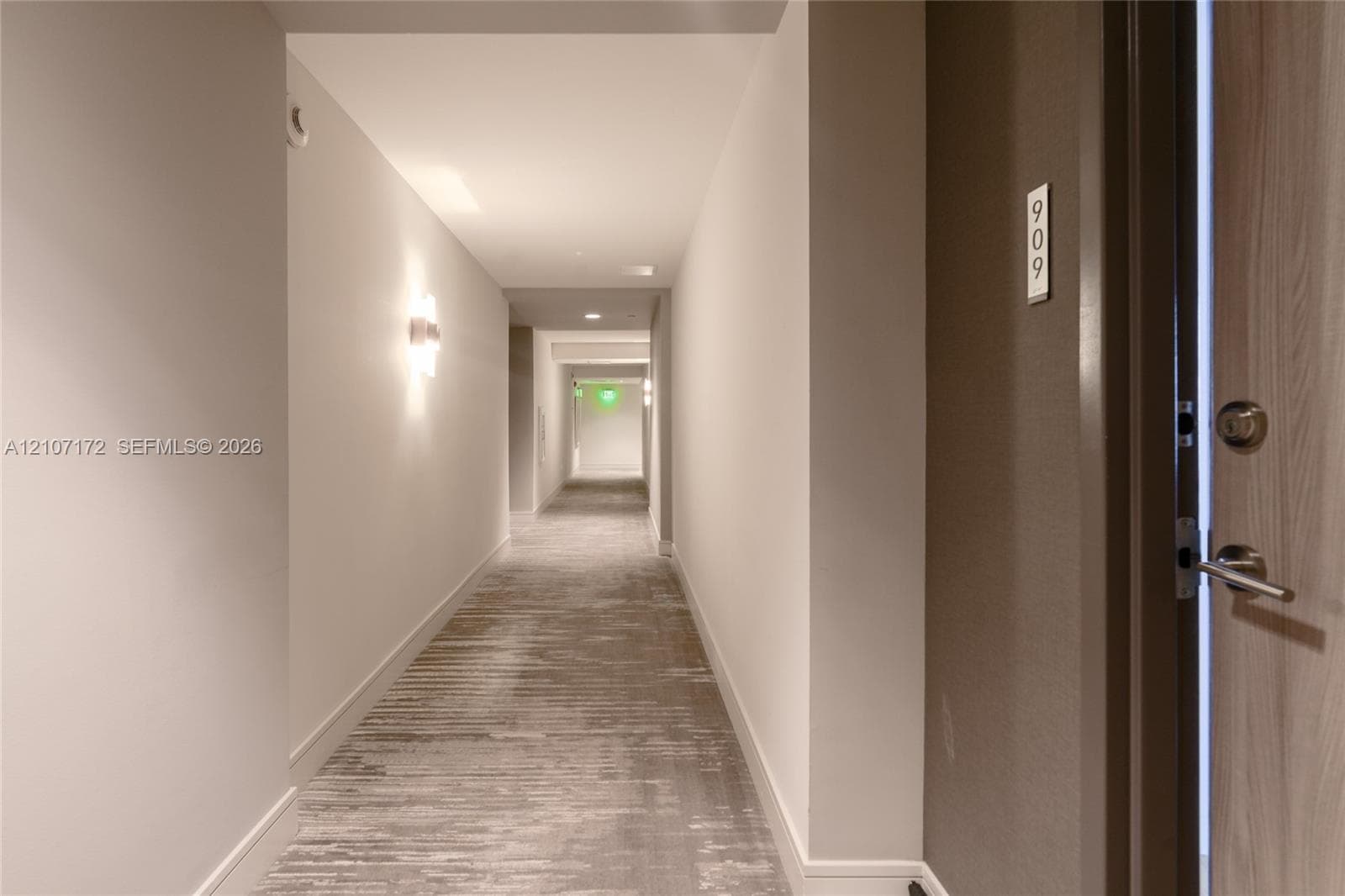 Interior hallway featuring neutral walls, wall-mounted sconce lighting, and textured carpeting