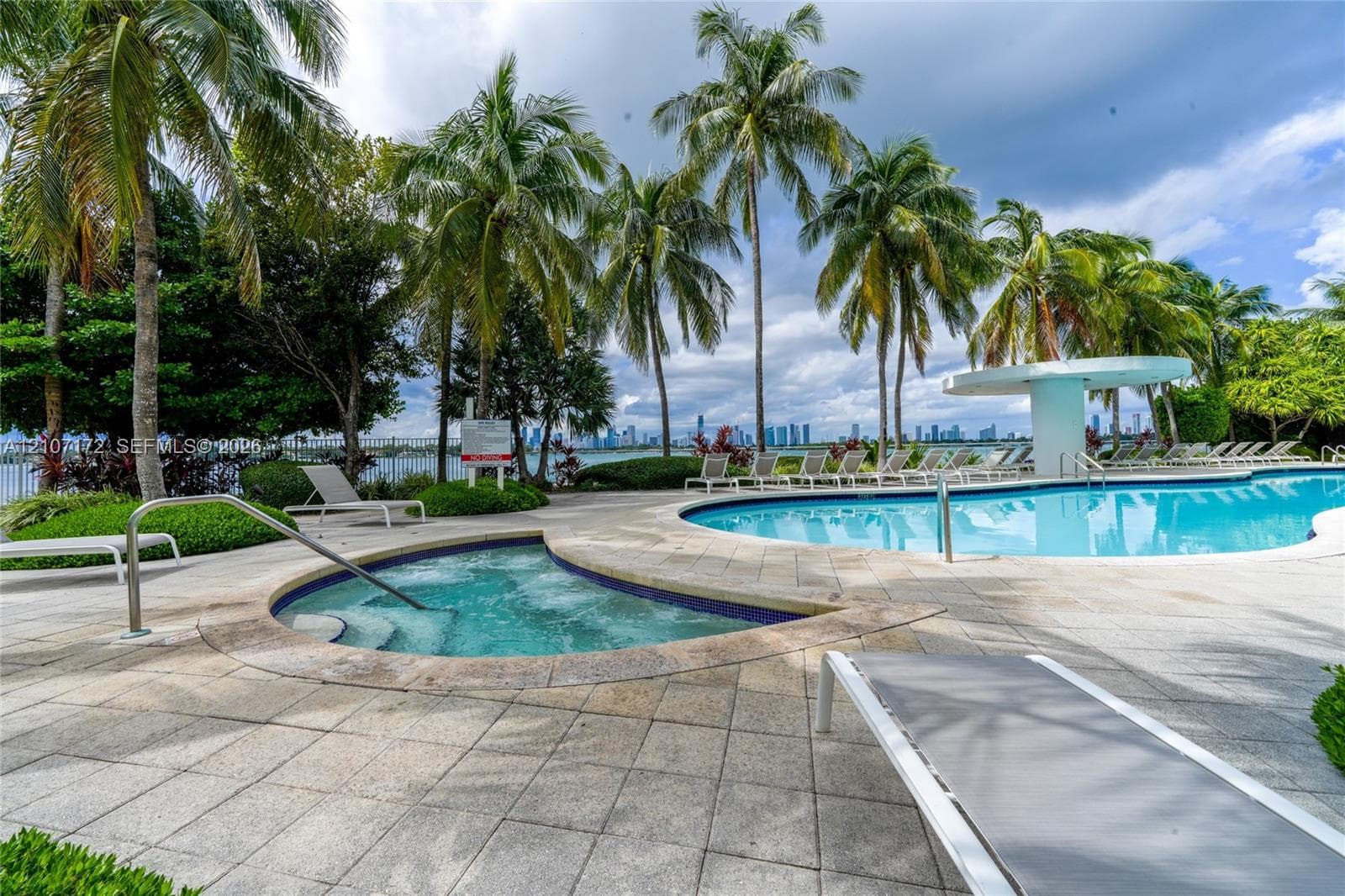 Outdoor swimming pool and attached spa featuring stone-paver decking, integrated shade structure, and mature palm landscaping