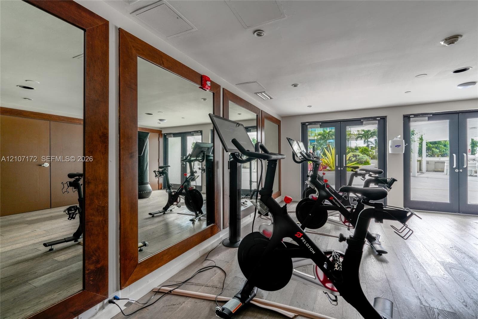 Fitness center featuring wood-finish flooring, full-length wall mirrors with wood frames, and glass-paneled double doors
