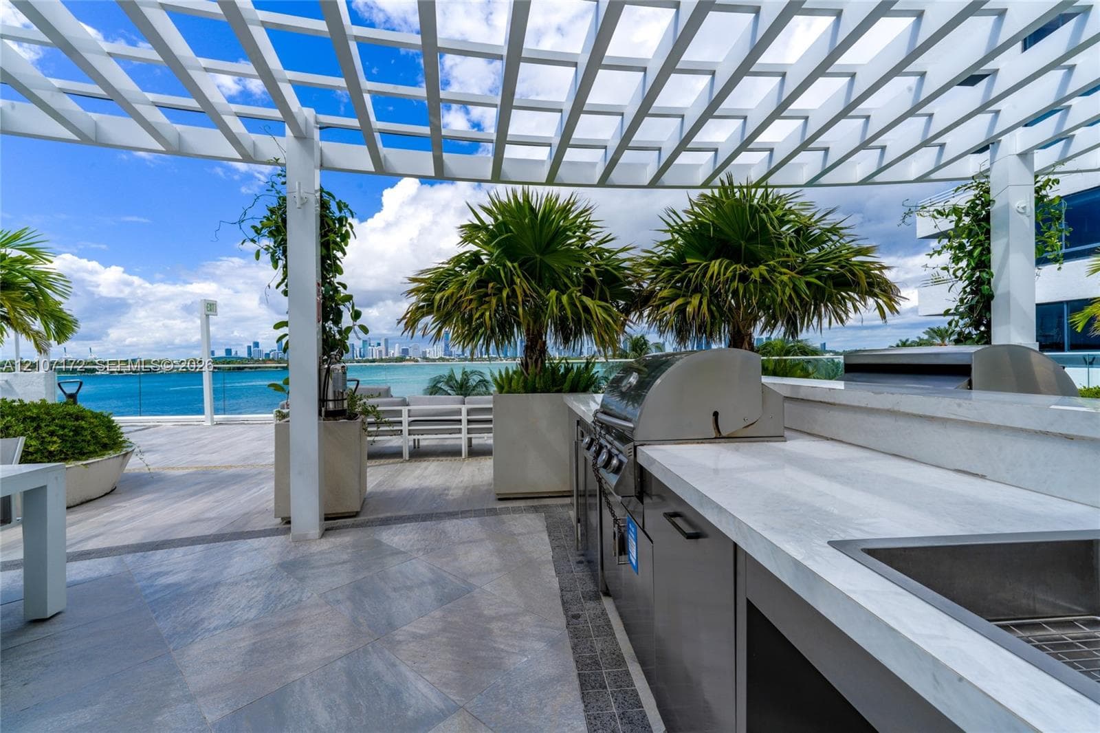 Outdoor terrace featuring a white pergola, stainless steel built-in grill, stone-surface countertop, and large planters