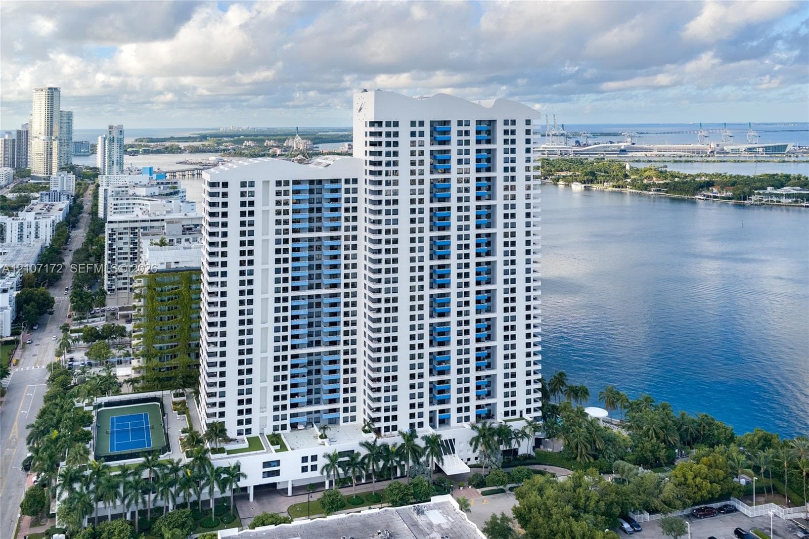 High-rise residential tower featuring multiple private balconies, a hard-surface tennis court, and immediate proximity to the waterfront