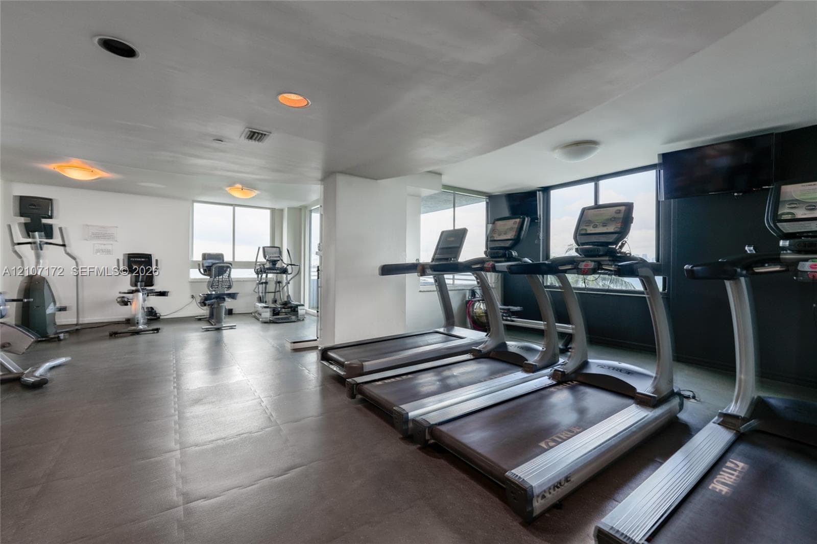 Fitness center featuring resilient rubberized flooring, recessed ceiling lighting, and large windows