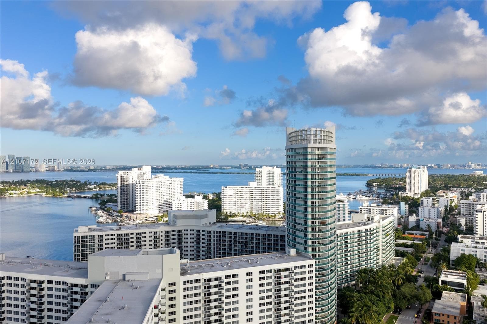 Aerial perspective featuring a glass-facade high-rise tower, expansive coastal waterfront, and urban skyline