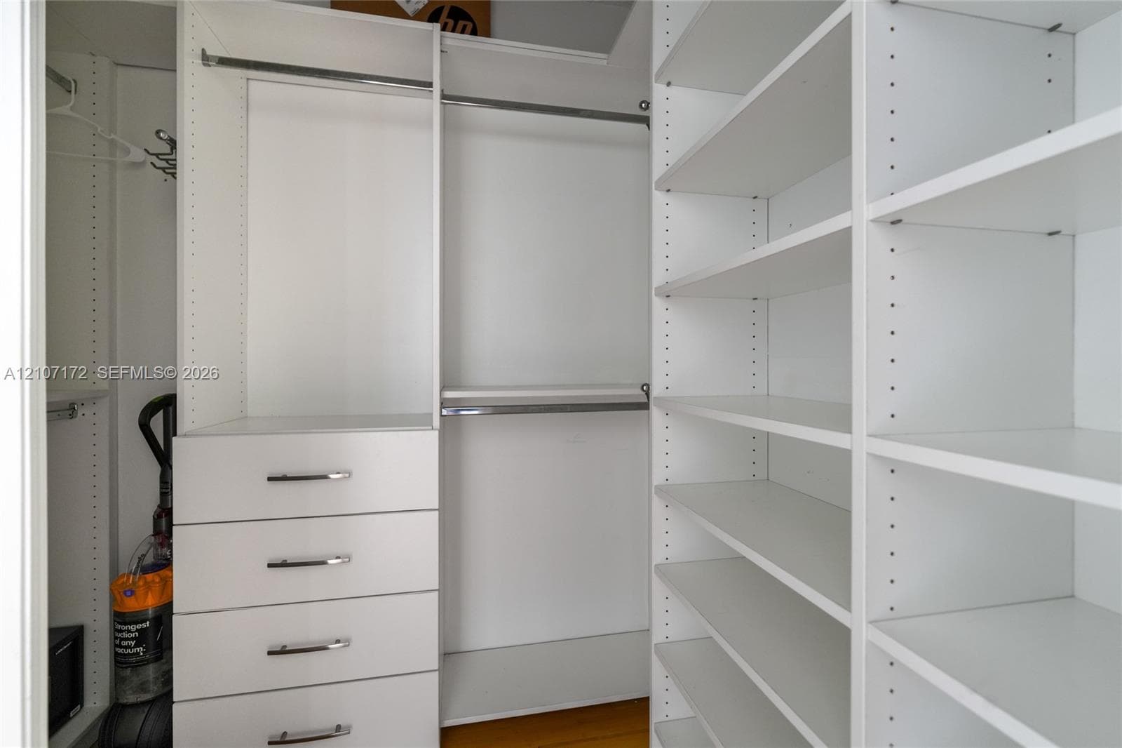 Custom walk-in closet featuring white laminate cabinetry, four soft-close drawers with metallic pulls, adjustable shelving, and dual-level metal hanging rods