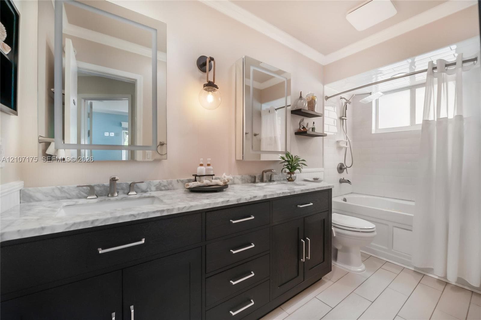 Hallway Bath. Double vanity featuring dark cabinetry, stone-finish countertops, lighted dual mirrored cabinets, wall-mounted lighting, and a bathtub-shower combination.