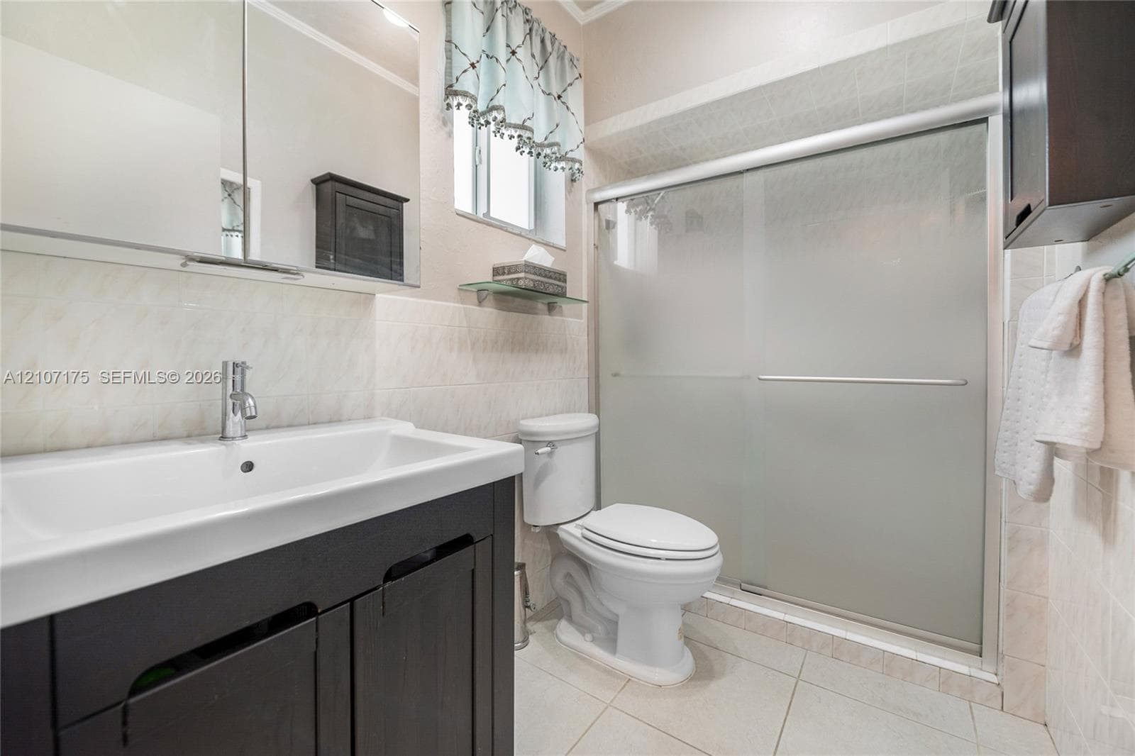 4th Bedroom En-Suite Bath. Dark wood-finish vanity with a rectangular sink, polished chrome faucet, tile-surround shower with frosted sliding glass doors.