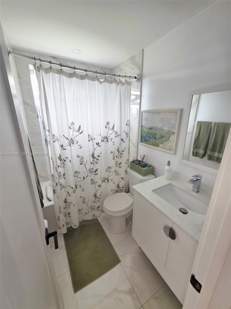 Bathroom featuring a vanity with a white composite countertop, an undermount sink, a chrome faucet, large-format tile flooring, and a tub-shower enclosure with tiled surround