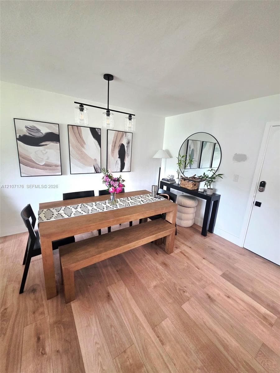 Light-toned wood-finish flooring and a contemporary three-light linear chandelier with clear glass shades