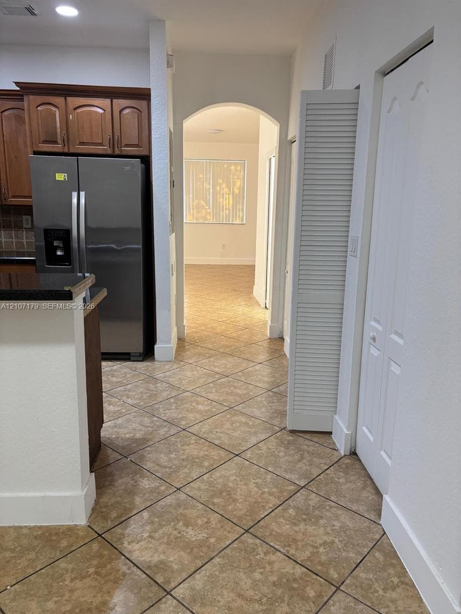Kitchen featuring wood cabinetry, stone-finish countertops, stainless steel appliance, diagonal tile flooring, and a structural archway