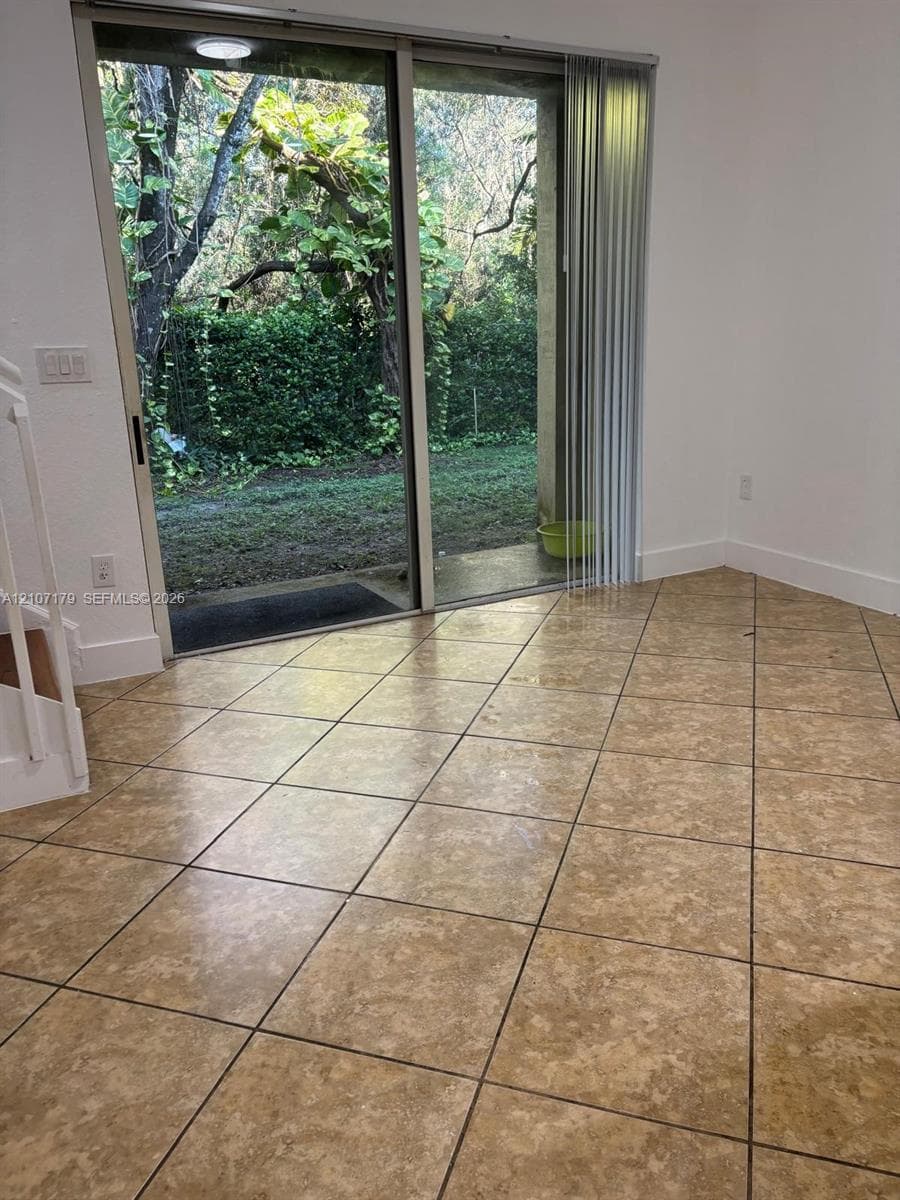 Large-format tile flooring, sliding glass door, and exterior access to a lawn with mature landscaping