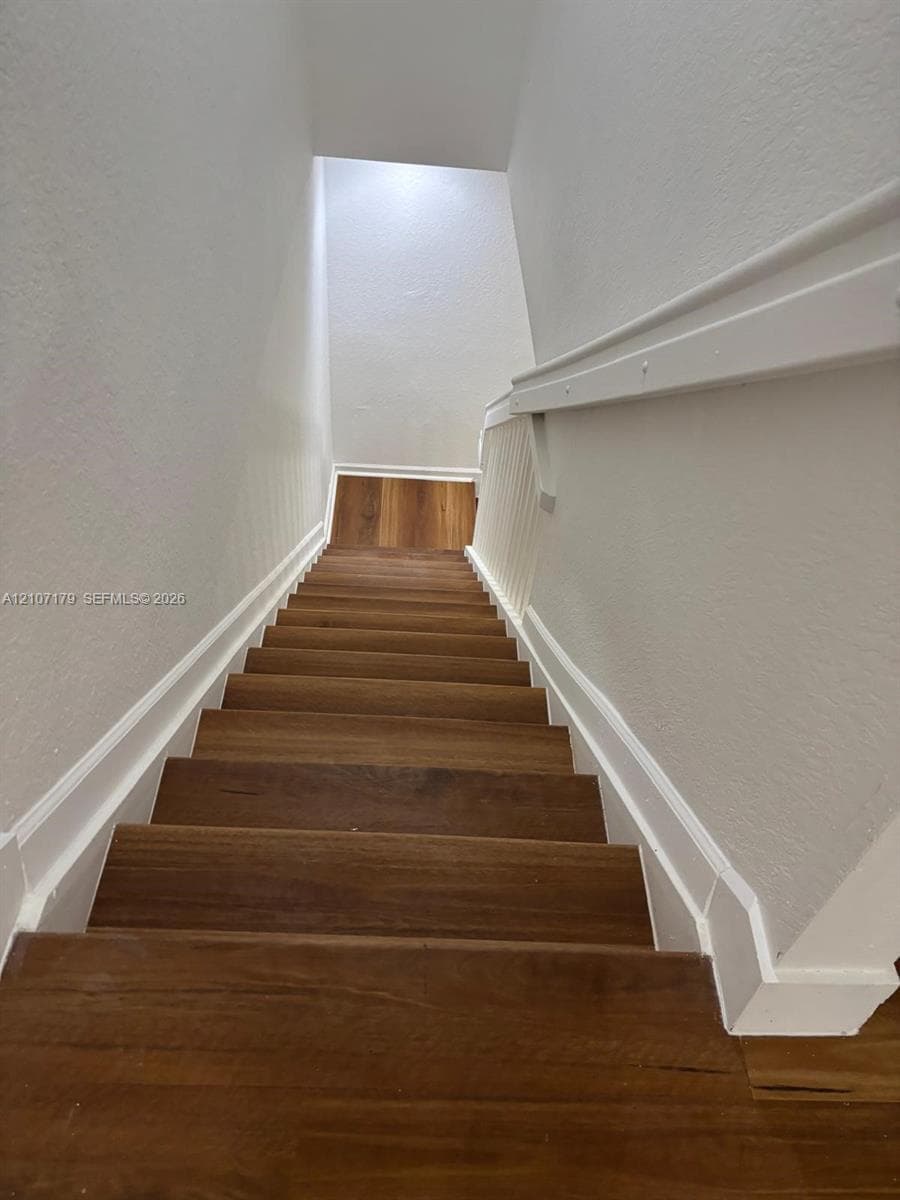 Staircase featuring wood-finish treads, white painted walls, and a matching white handrail