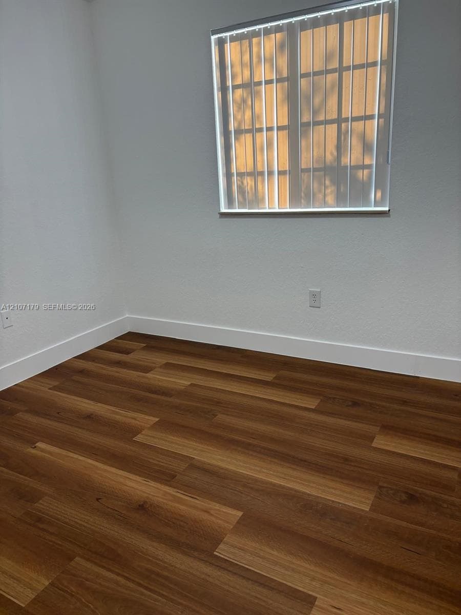 Wood-finish flooring, neutral wall tones, and window featuring vertical blinds