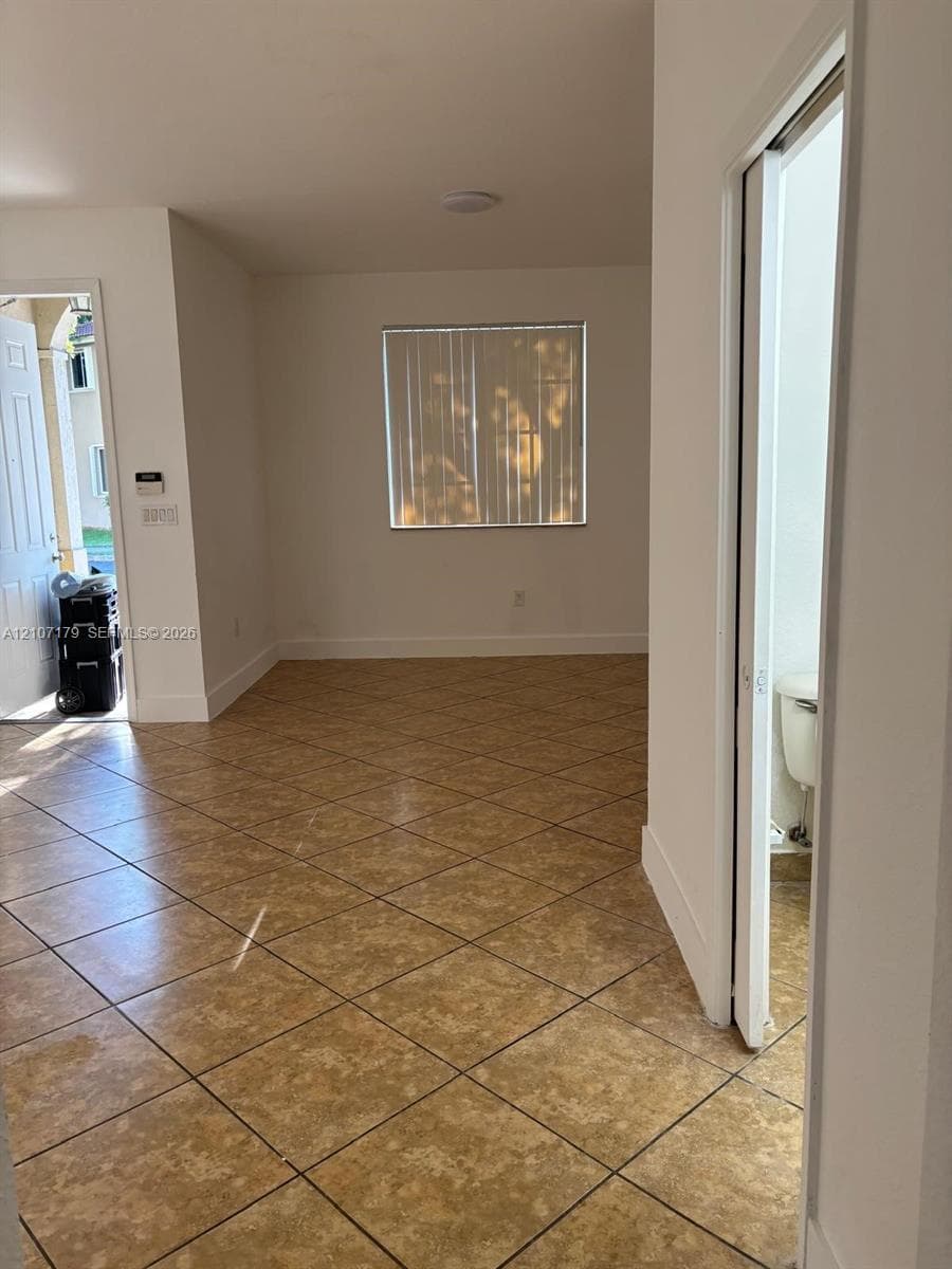 Neutral-toned ceramic tile flooring laid on a diagonal, crisp white interior wall finish, and a window with vertical blinds
