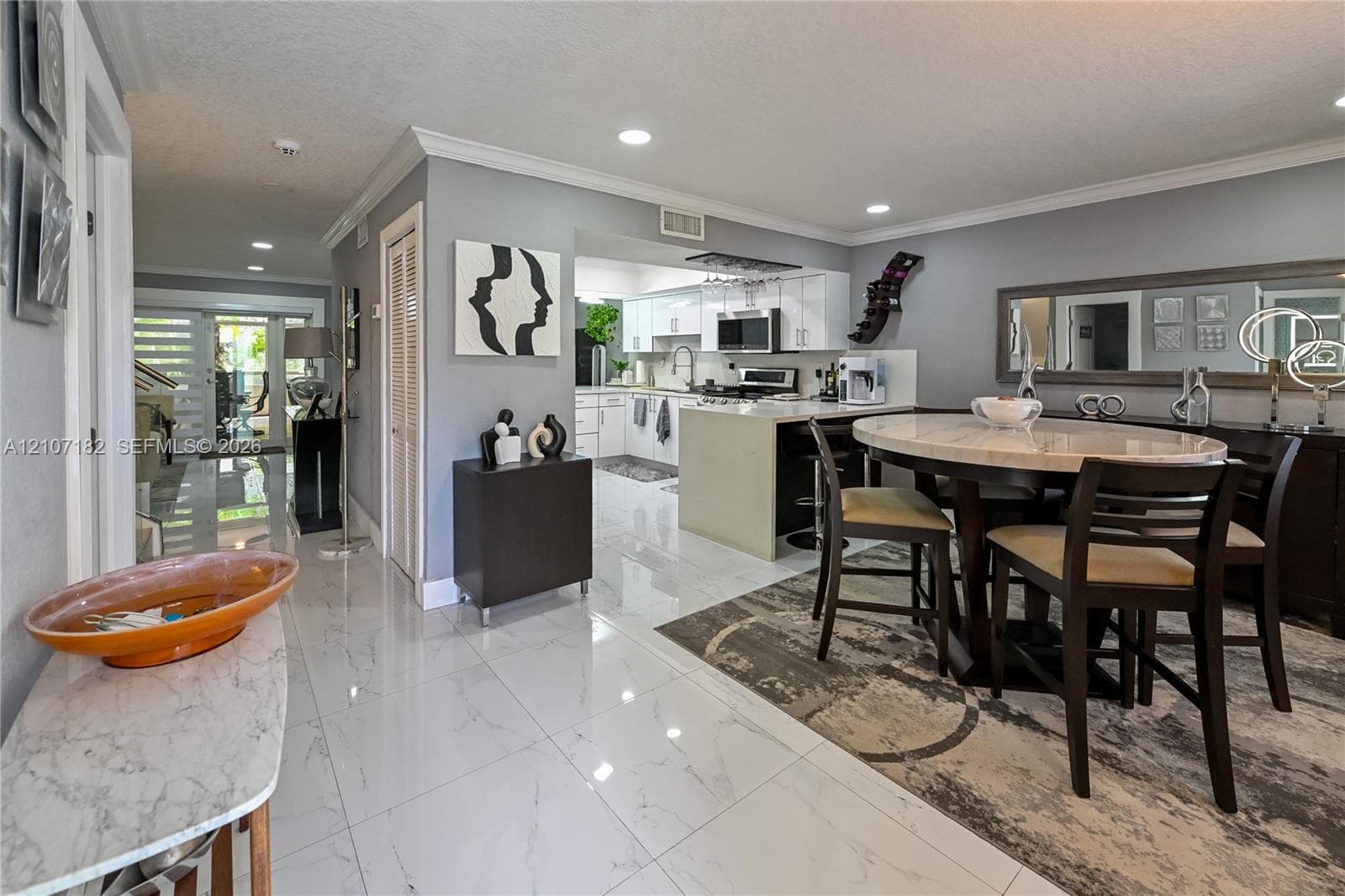 Open-concept interior featuring large-format polished tile flooring, recessed lighting, crown molding, and an island kitchen with white cabinetry