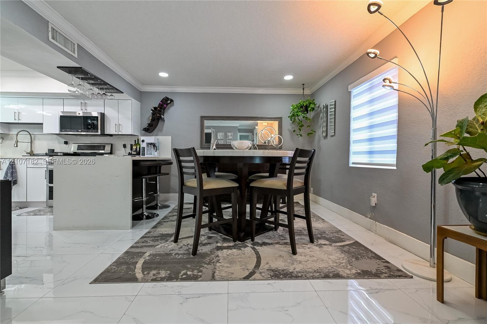 Polished stone-finish tile flooring, white gloss cabinetry, quartz countertop, recessed ceiling lighting, and horizontal tiered window shades