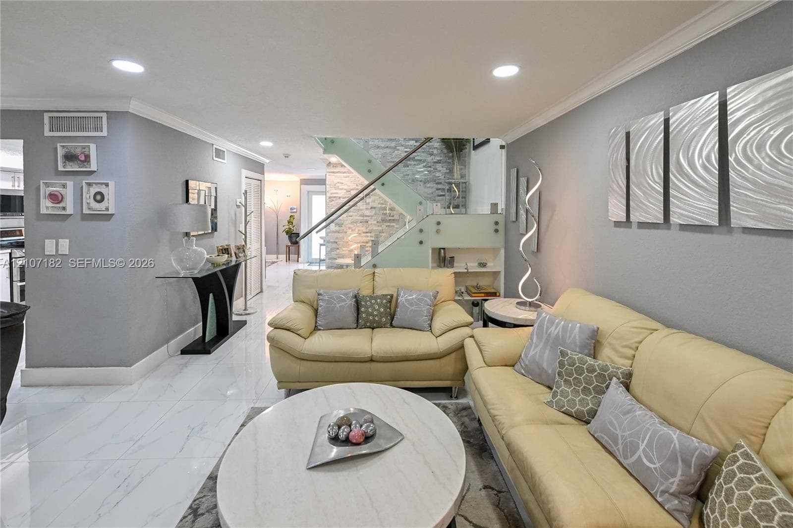 Large-format polished tile flooring, staircase featuring glass panel railings, and floor-to-ceiling stone accent wall