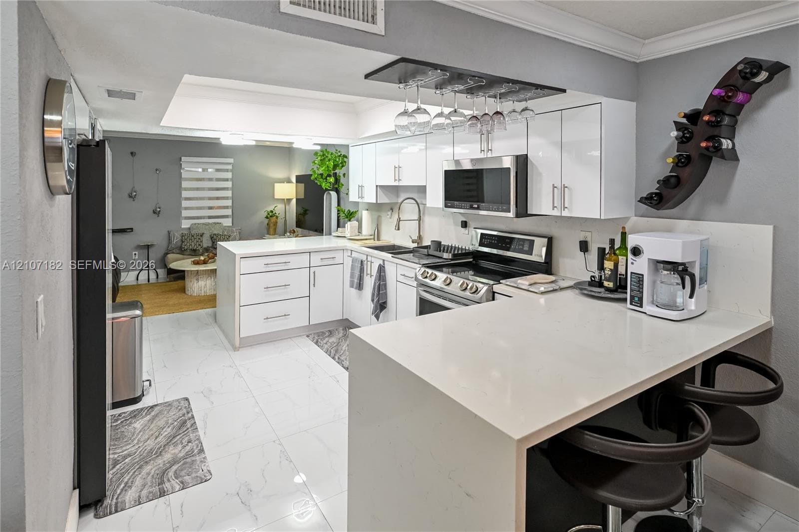 Kitchen featuring white high-gloss cabinetry, quartz countertops, a peninsula with breakfast bar seating, stainless steel appliances, and large-format tile flooring