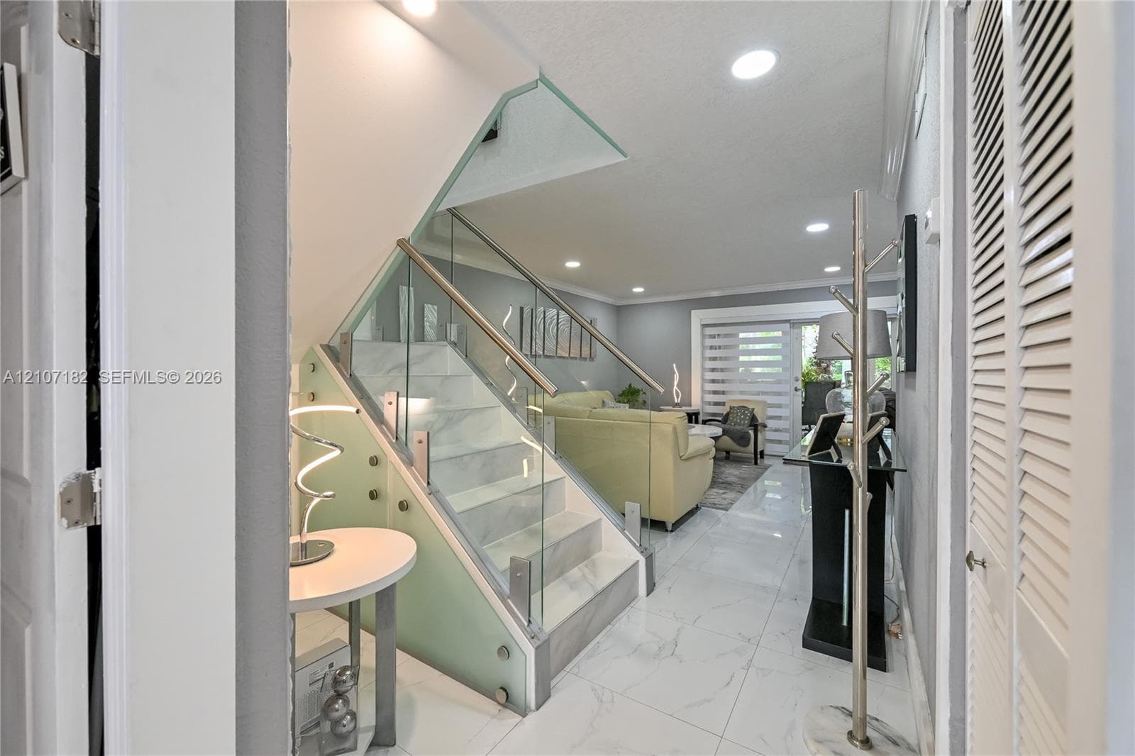 Staircase featuring white stone-finish steps, glass balustrade, and stainless steel handrail, complemented by large-format white tile flooring and recessed ceiling lighting