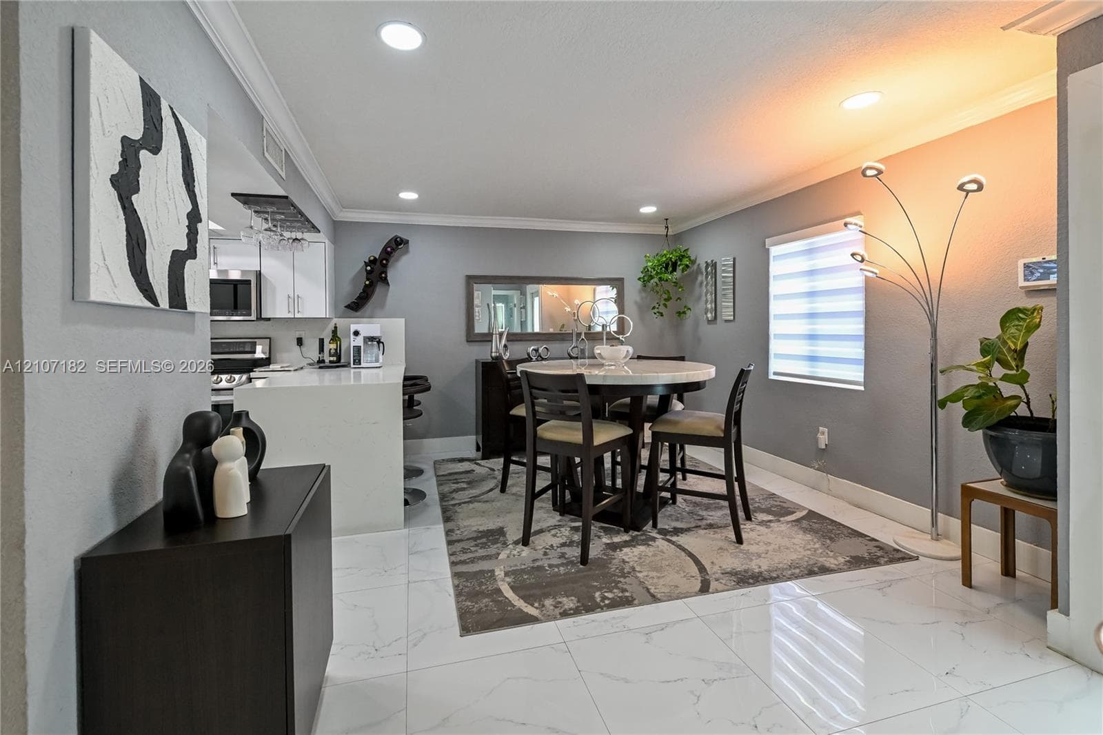 Large-format tile flooring, recessed lighting, crown molding, and a kitchen island with a light-toned countertop