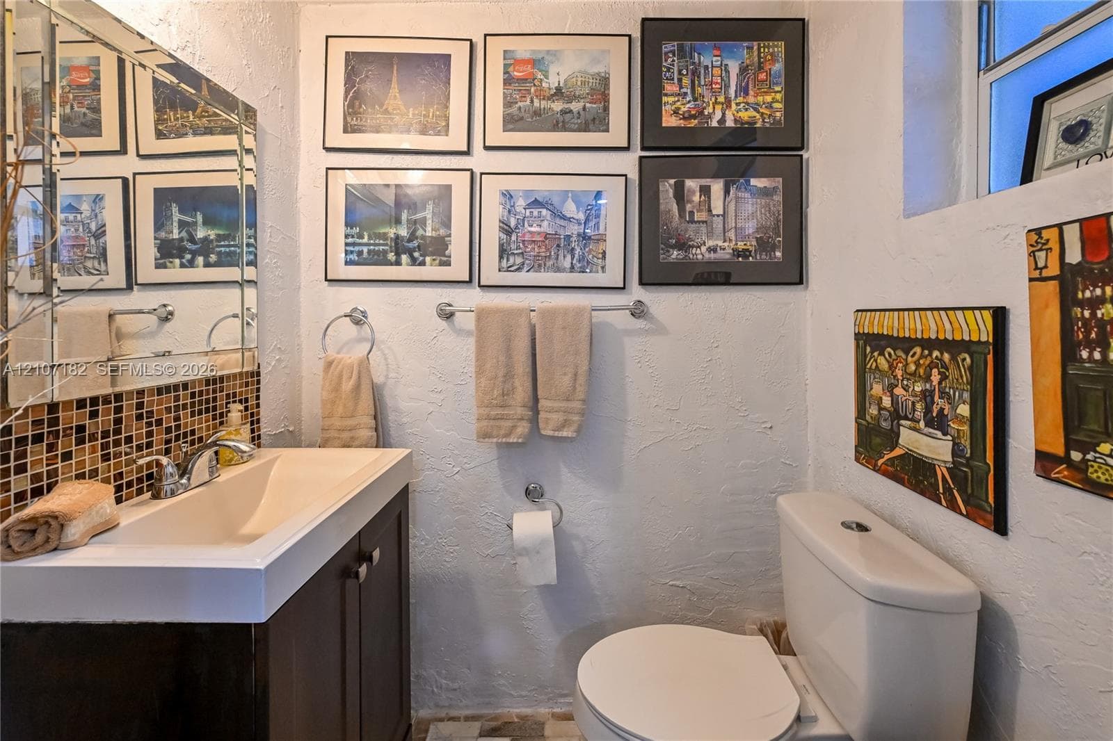 Bathroom featuring a dark-finish vanity with a rectangular integrated sink, chrome-finish faucet, multi-colored square mosaic tile backsplash, and large wall-mounted mirror